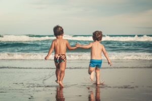 unrecognizable little boys holding hands and walking on sandy seashore